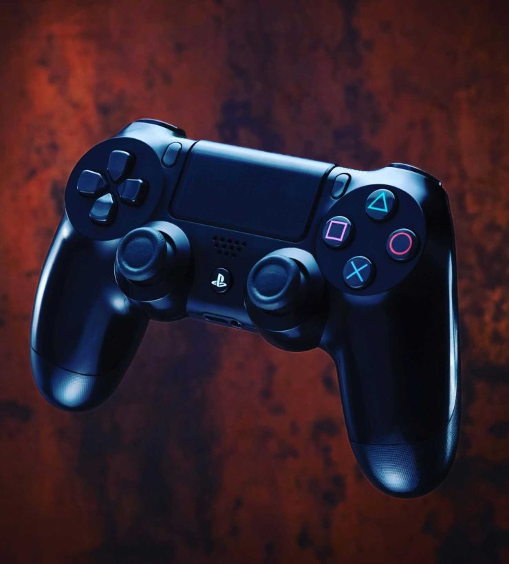 Modern PlayStation controller with glowing buttons on a dark textured backdrop.