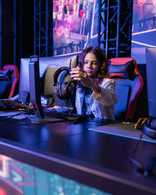 A young woman in a gaming chair adjusting headphones in an esports arena.