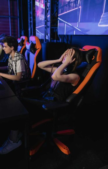 Woman covering eyes in gaming chair at esports event, expressing frustration after a loss.