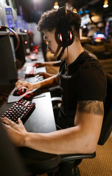 A gamer wearing headphones intensely focused on gaming in a cyber-themed arcade.