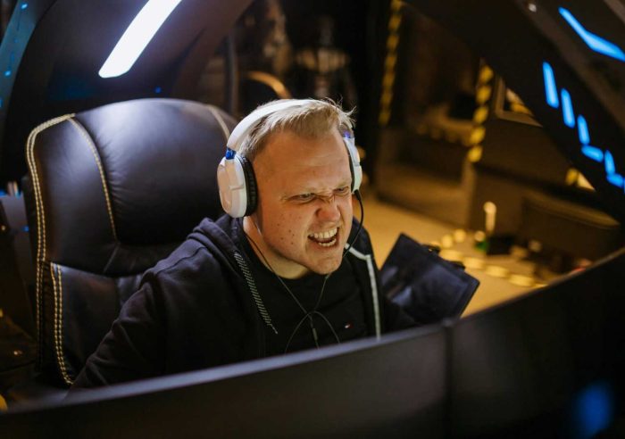 A passionate gamer celebrating victory while gaming indoors with white headphones and a gaming chair.