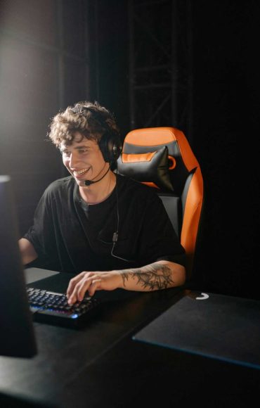 Smiling young man playing games on PC with headphones, enjoying a thrilling gaming session.